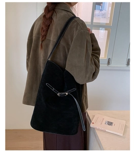 Detail of black suede bucket bag with leather buckle strap and elegant metallic hardware