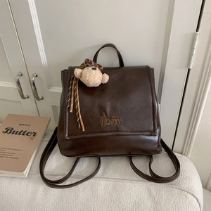 Detail of vintage dark brown PU leather backpack with IBM embroidery and plush bear charm
