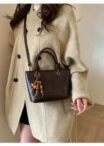 Dettaglio della borsa a secchiello marrone vintage con ciondolo in legno su cappotto di lana