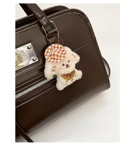 Close-up of white plush dog charm with orange checkered hat on brown leather bag