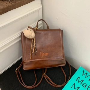 Detail of vintage brown leather backpack featuring a plush bear charm and jbm logo