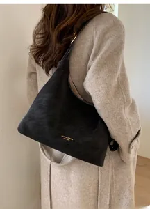 Macro shot of a black suede hobo bag with gold letter printing worn by a model