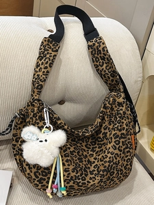 Grand sac hobo léopard avec bandoulière large et breloque ours sur un canapé blanc