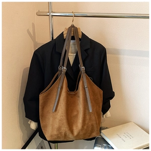 Close-up of caramel suede tote bag with adjustable straps on a black blazer background