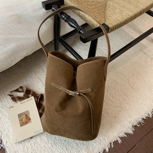 Detail shot of brown suede bucket bag with leather strap and metal buckle on a cozy rug