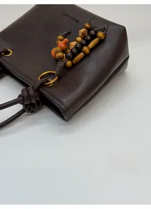 Detailed close-up of dark brown matte leather bag with wood bead and gourd pendant charms