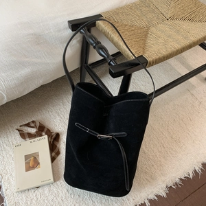 Detailed shot of black suede bucket bag with white contrast stitching and buckle detail