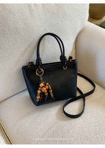 Detail of vintage black bucket bag with wooden bead charm on a soft beige fabric sofa