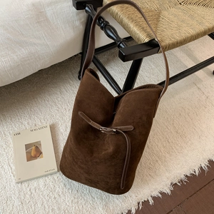 Detail view of dark brown suede bucket bag with contrast stitching on elegant chair