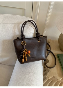 Close-up of vintage brown leather bucket bag with beaded tassel and embossed fashion text