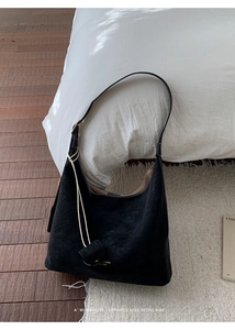 Detail of a black suede Hobo bag with minimalist gold lettering on soft white bedding