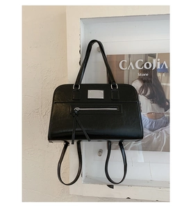 Detailed close-up of a minimalist black leather handbag with silver metallic hardware accents