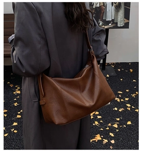 Brown leather tote bag worn by a model in a fall setting with yellow leaves