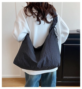 Black and blue checkered hobo bag with pleated strap shown on shoulder for daily commute