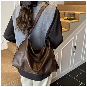 Detail of soft brown leather tote bag worn as a shoulder hobo bag in a modern room
