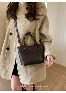 Dettaglio borsa a tracolla marrone in pelle opaca indossata su un cappotto beige