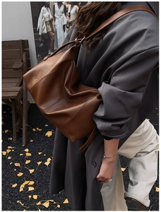 Side view of caramel brown leather tote bag worn on shoulder in autumn setting