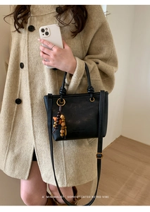 Borsa a secchiello minimalista in pelle nera con ciondolo in legno su cappotto beige
