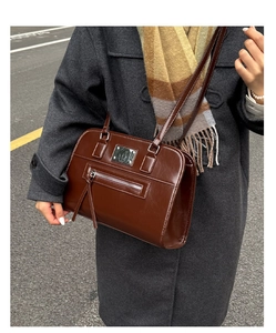 Detail of vintage brown glossy tote bag with dual straps and stylish zipper on grey coat