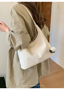 Detail view of large cream white leather hobo tote bag worn with a camel coat in a chic room