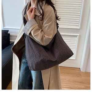Model wearing a large checkered tote bag with a khaki trench coat for a casual look