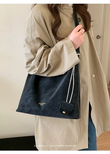 Detail of a black vintage leather tote bag with gold lettering shown on a khaki coat