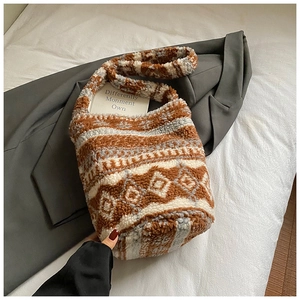 Détail du sac seau en peluche à motifs ethniques sur un lit blanc avec blazer gris