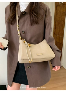 Close-up of beige leather shoulder bag with tassels styled on a dark brown coat