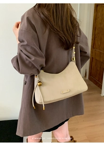 Detail of cream leather hobo bag featuring golden hardware and decorative charm