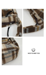Close-up of tartan pattern fabric with zipper details and shoulder strap on a plaid tote