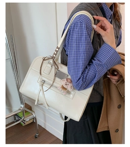 Detail of a cream faux leather tote bag with ribbon bow and plush dog charm on shoulder