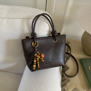 Dettaglio borsa tote marrone con nappine in perline di legno su tessuto bianco