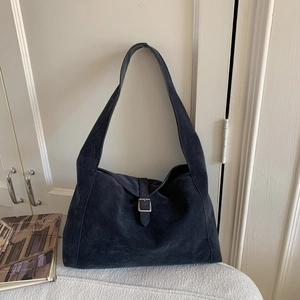 Close-up of matte suede hobo bag with silver buckle strap on a white surface