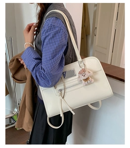 White minimalist tote bag with silver zippers, plush charm, and long tassel accents