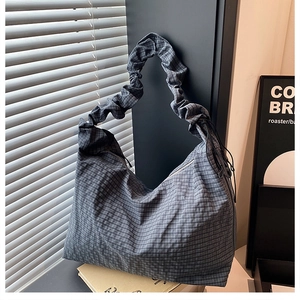 Detail of grey checkered hobo bag with scrunchie strap and drawstring on books