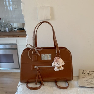 Brown leather handbag detail featuring a stylish check ribbon bow and plush dog charm