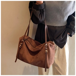 Detail of suede shoulder bag featuring adjustable straps and elegant gold buckles