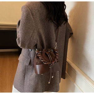 Detail of dark brown bucket bag with woven handle and drawstring on a model