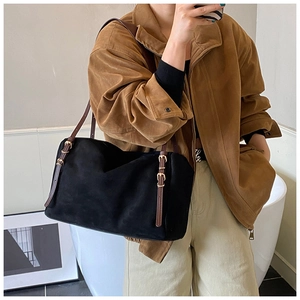 Detail of black suede tote bag showing adjustable brown leather strap and gold buckles