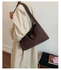 Deep brown suede tote bag with silver buckle and wide strap worn over a beige coat