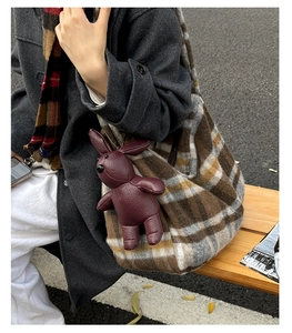 Close-up of a burgundy leather rabbit pendant on a brown plaid wool tote bag