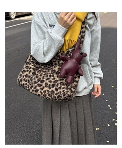 Street style view of a plush leopard print tote bag with a burgundy bear charm detail