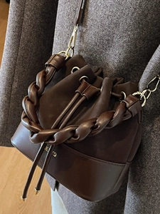 Minimalist deep brown leather bucket bag with woven handle and gold metal hardware hooks