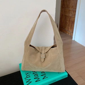 Close-up of khaki suede hobo bag with silver buckle on a blue design book background