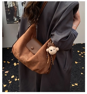 Detail of a brown suede crossbody bag featuring delicate line embroidery and a plush bear charm