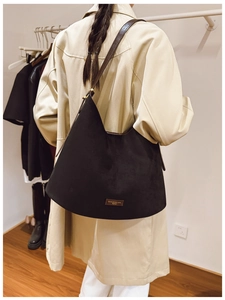 Detail of black suede tote bag with brown leather strap and gold logo plate