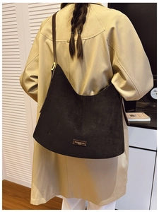 Detail of black suede bucket bag with brown leather strap and gold logo plate