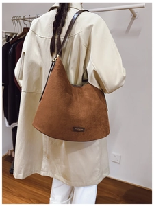 Brown suede hobo bag shown from back view on model wearing a beige trench coat