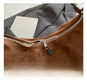 Close-up of brown suede shoulder bag with premium silver zippers and metal hardware details