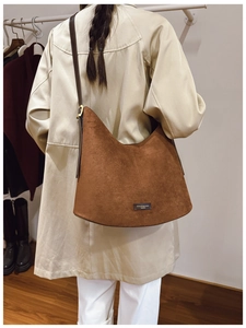 Brown suede hobo bag with adjustable leather strap worn by model in showroom